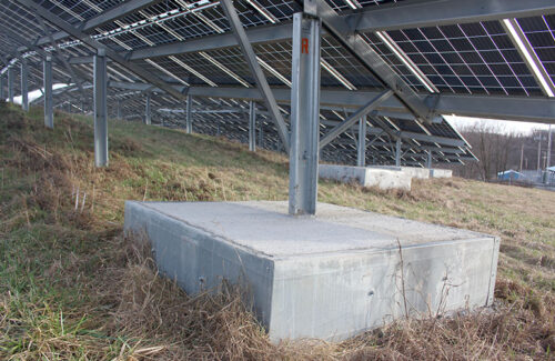 A rectangular concrete ballast acts as the foundation for a post at the end of a solar panel row.